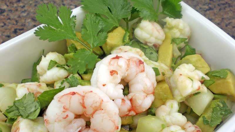 A photograph of argentine red shrimp ceviche with shrimp, diced avocado, cilantro, cucumber and onion.