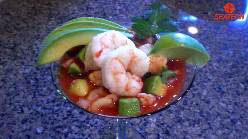 A photograph of a Mexican shrimp cocktail featureing Argentine red shrimp, avocados, onions, cucumbers, cilantro, tomato juice and clam juice.